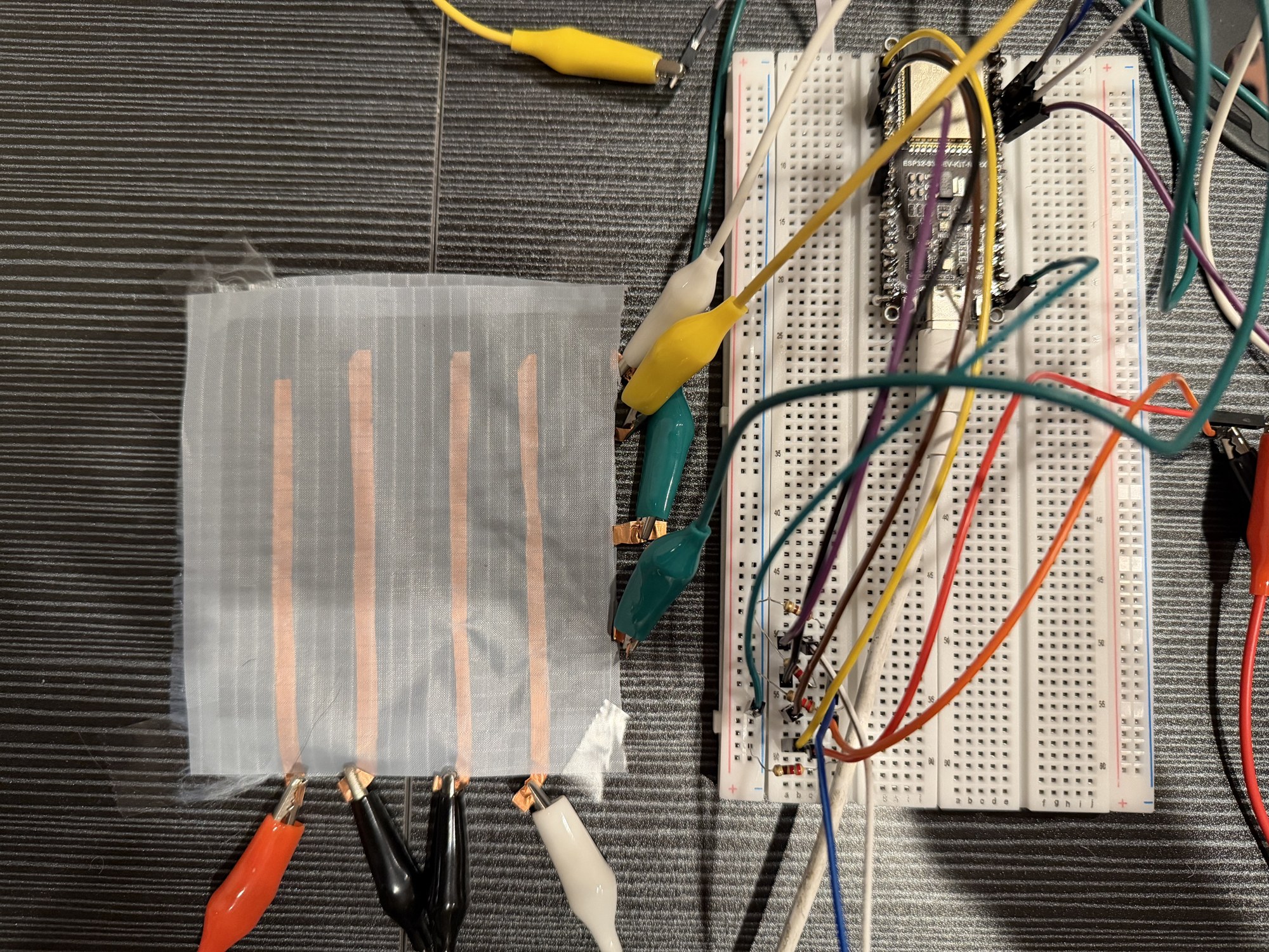 Parallel metal strips on a flexible sheet connected by wires to breadboard electronics.