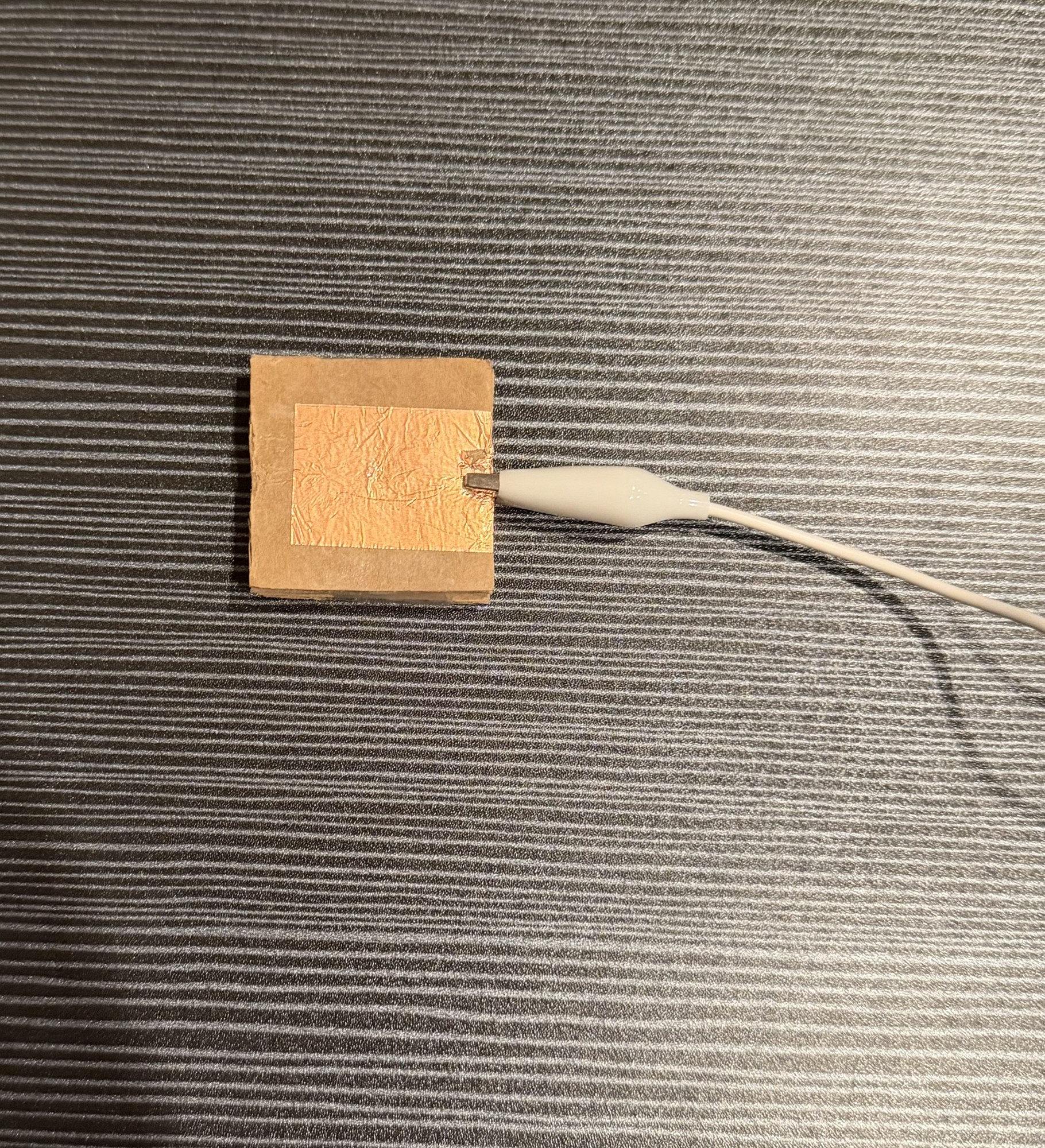 Small sensor-material sample on a worktable with an alligator clip test lead attached.